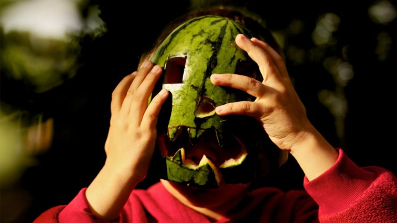 Foto eines Kindes mit Wassermelone als Jack-O-Laterne-Maske vor dem Gesicht