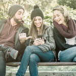 Geschenke-App givie steht ab sofort auf Google Play zum Download bereit - Ein Mann und zwei Frauen auf der Parkbank, lachend auf ein Smartphone schauend