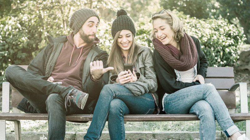 Geschenke-App givie steht ab sofort auf Google Play zum Download bereit - Ein Mann und zwei Frauen auf der Parkbank, lachend auf ein Smartphone schauend